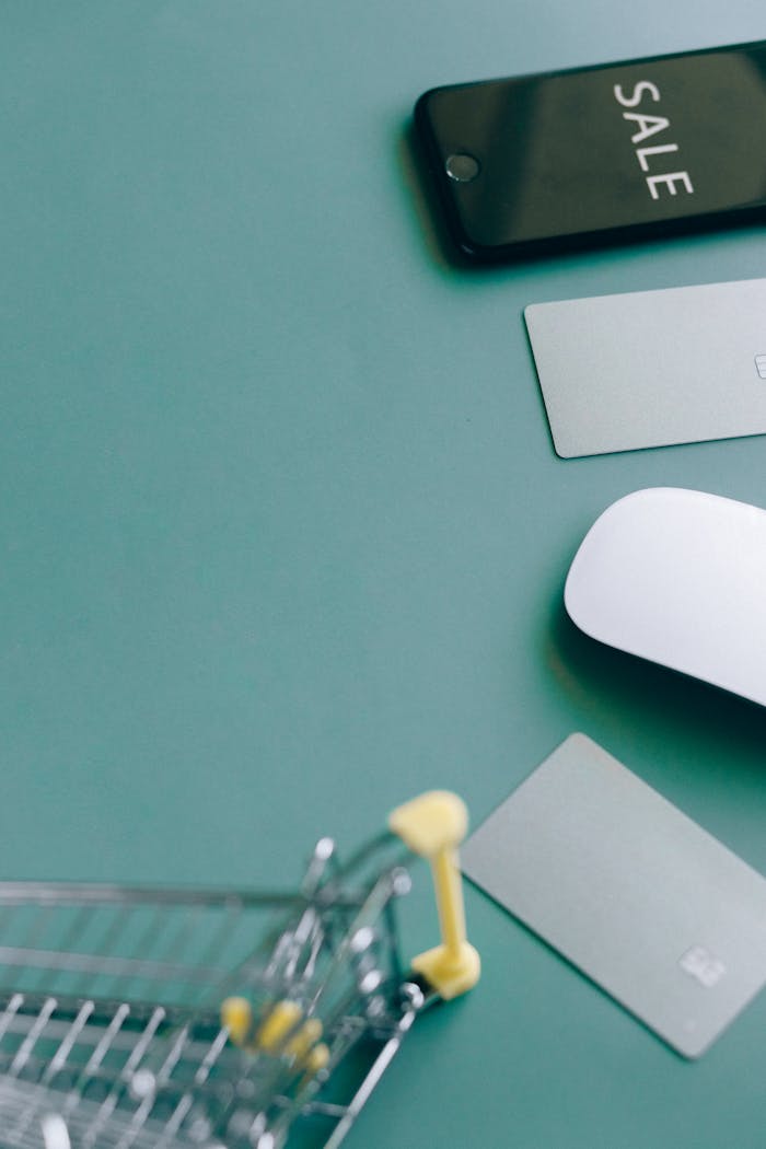 Flat lay of a shopping cart, phone with SALE display, and payment cards on a green background.